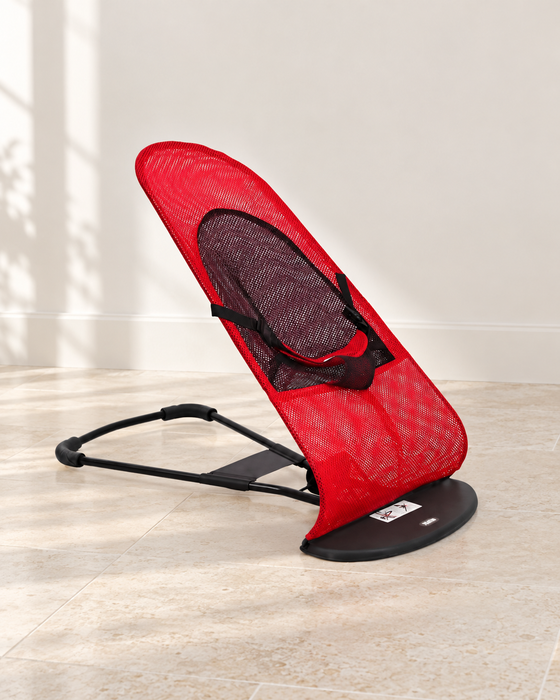 Red and black mesh rocking chair in an ivory room.