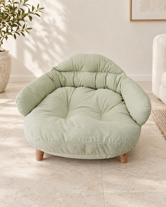 Pale green corduroy pet bed with wooden feet on an ivory stone floor.