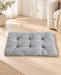 Grey tufted rectangular pet mat on a light wooden floor in a softly lit living room.