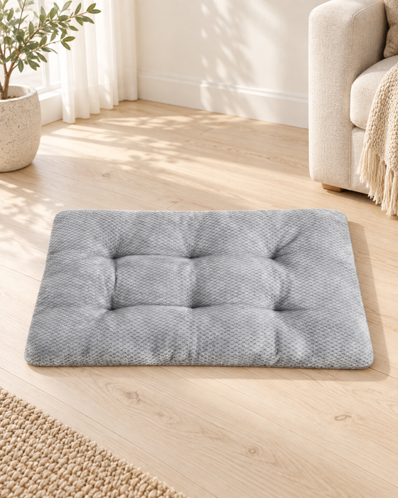 Grey tufted rectangular pet mat on a light wooden floor in a softly lit living room.