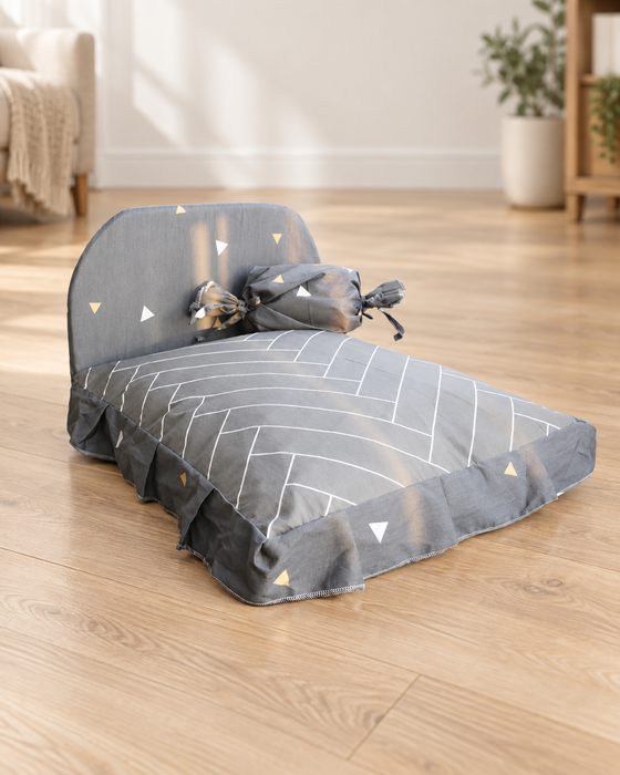 Grey pet bed with geometric white lines, triangle motifs and a tied bolster in a living room.