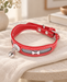 Red pet collar with white stitching, a silver-tone bone ornament and bell on ivory linen.