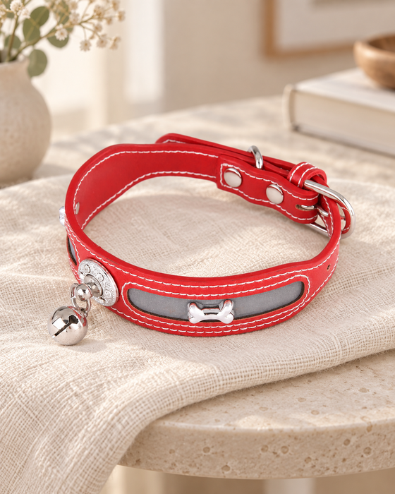Red pet collar with white stitching, a silver-tone bone ornament and bell on ivory linen.
