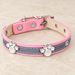 Pink and grey collar with silver paw decorations resting on pale stone