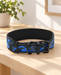 Blue and black camouflage dog collar with black buckle and ring on a light wooden bench.