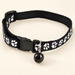 Black paw-print pet collar with bell on ivory background