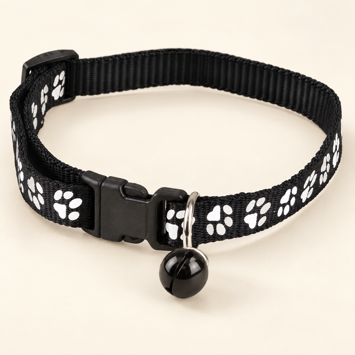 Black paw-print pet collar with bell on ivory background