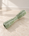 Sage-green textured dog chew toy resting on an ivory stone floor.
