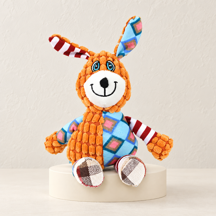 Orange patchwork rabbit dog toy displayed on an ivory plinth.