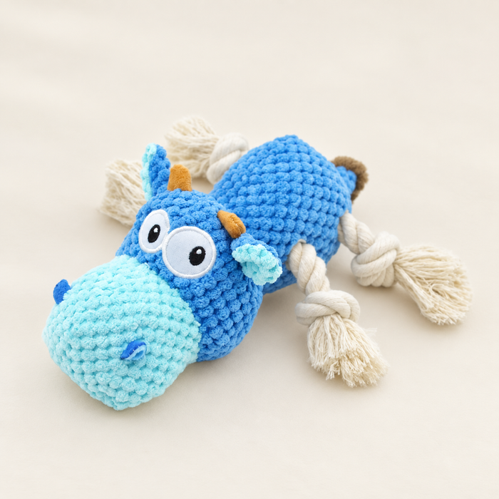 Blue cow dog toy with knotted rope legs resting on an ivory surface.