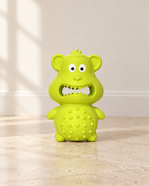 Lime-green rubber monkey dog toy on an ivory stone floor.