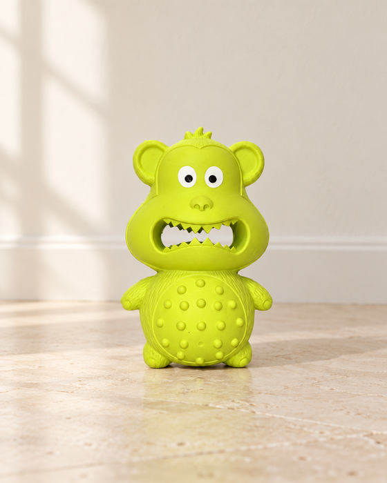 Lime-green rubber monkey dog toy on an ivory stone floor.