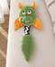 Green and orange dragon plush dog toy with a black-and-white fabric connector on ivory linen.
