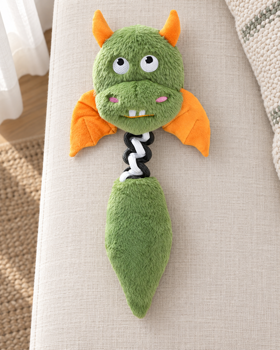 Green and orange dragon plush dog toy with a black-and-white fabric connector on ivory linen.