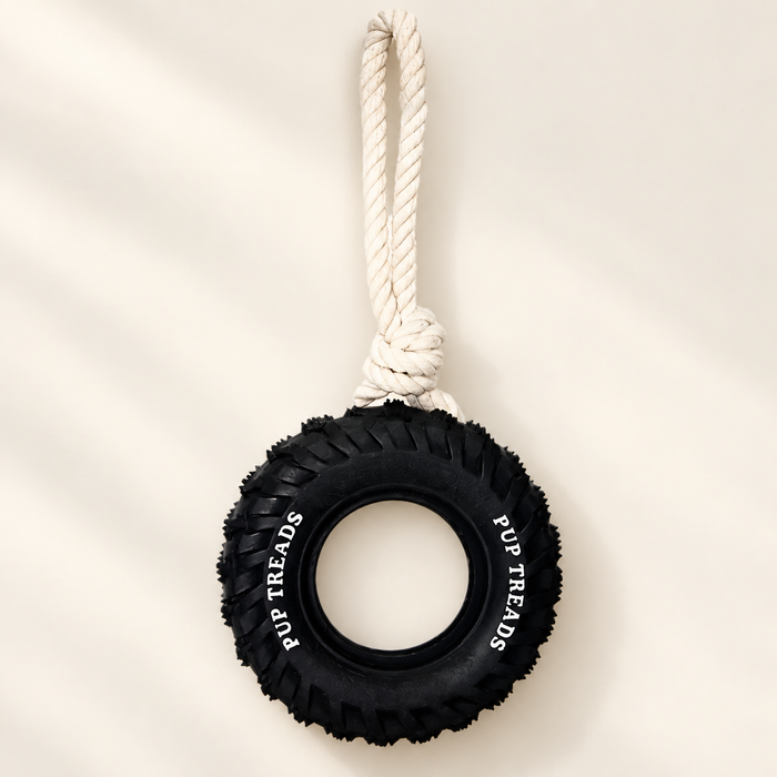 Black tyre dog toy with white rope handle on ivory surface