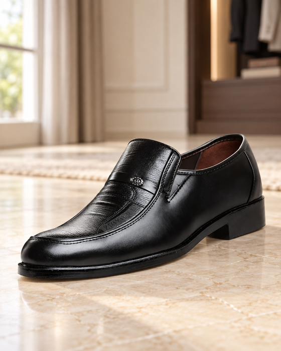 Black slip-on dress shoe with an apron seam, a small metal emblem and a low heel in a dressing room.