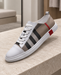 White and taupe low-top sneaker with a checked side panel and red heel accent on a pale stone bench.