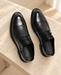 Pair of black lace-up dress shoes with curved toe seams on a pale stone bench.