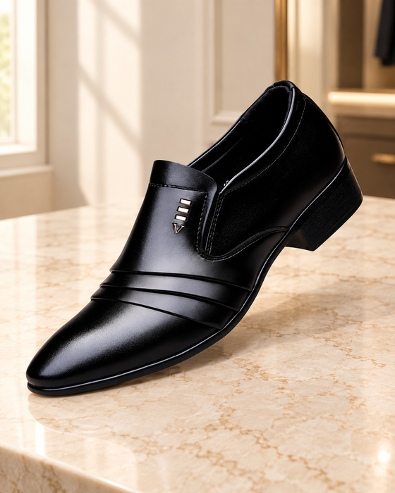 Black pointed-toe slip-on dress shoe with three gold bars and a V ornament on a pale stone surface.