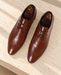 Pair of brown lace-up dress shoes with wooden shoe trees on a pale stone bench.