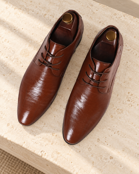 Pair of brown lace-up dress shoes with wooden shoe trees on a pale stone bench.