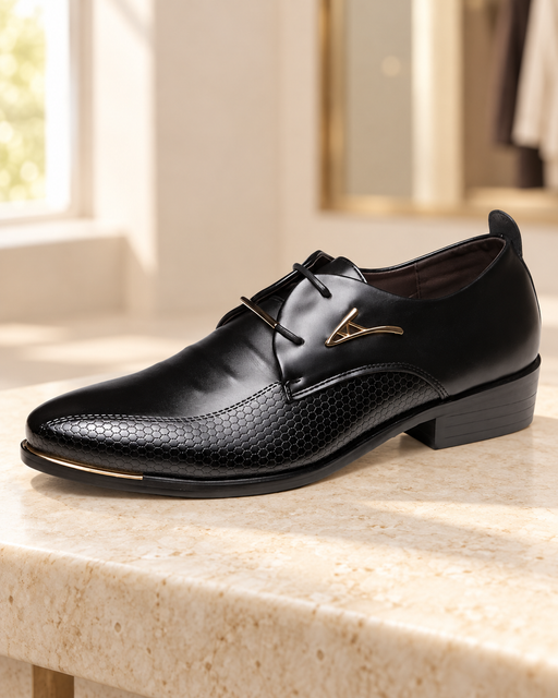 Black dress shoe with a honeycomb-textured panel and gold ornament on a pale stone bench.