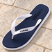 Navy flip-flop with white straps and white sole edge on pale stone patio paving.