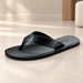 Black flip-flop sandal with stitched straps resting on an ivory floor.