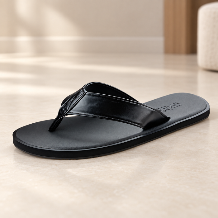 Black flip-flop sandal with stitched straps resting on an ivory floor.