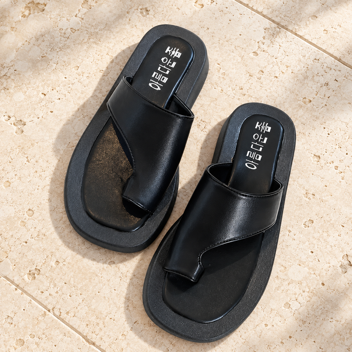 Black asymmetrical sandals on an ivory stone terrace.