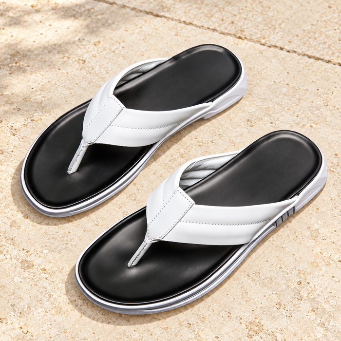 White thong sandals with black footbeds on warm stone.