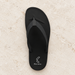 Black flip-flop with its original silver heel mark on ivory stone.
