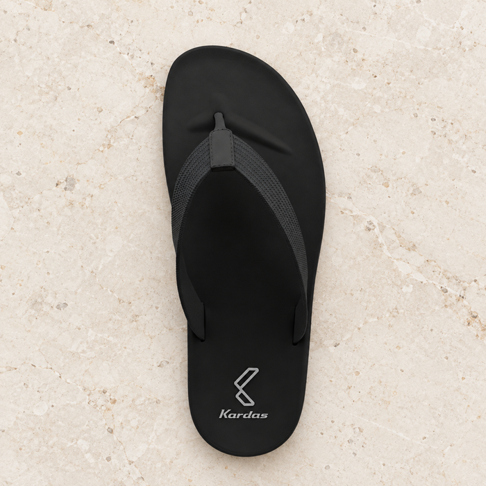 Black flip-flop with its original silver heel mark on ivory stone.