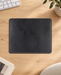 Black rectangular mouse pad with pale edge stitching on a light wood desk.