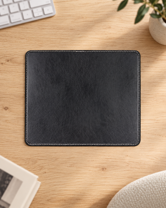 Black rectangular mouse pad with pale edge stitching on a light wood desk.