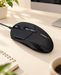 Black wired mouse on a warm ivory desk beside a monitor.