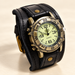 Antique brass-tone watch with black leather cuff on ivory surface