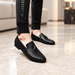 Black woven tassel loafers worn on an ivory stone floor.