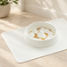 Off-white slow-feeder bowl with raised shapes on a mat in a softly lit home.