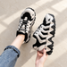Black and ivory chunky lace-up shoes, one worn and one held above an ivory floor.