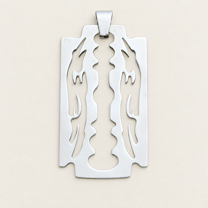 Silver blade-shaped decorative pendant without a chain, lying on an ivory surface.
