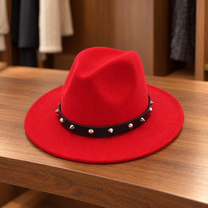 Red fedora with a black band and alternating silver studs on a wooden shelf.