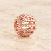 Rose-gold openwork bead resting on ivory stone