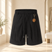 Black drawstring shorts with an orange and gold pendant in an ivory dressing room