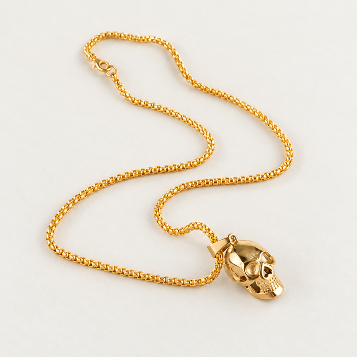 Gold-tone skull pendant necklace with complete chain on an ivory surface