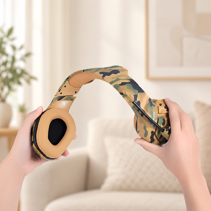 Tan camouflage headphones held open by two hands in a softly lit interior.