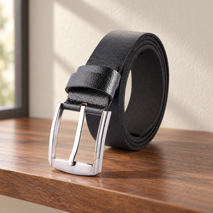 Black rolled belt with a silver pin buckle on a walnut shelf.