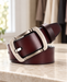 Rolled burgundy-brown leather belt with a silver rectangular buckle on a pale stone dressing table.