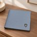 Blue-grey bifold wallet with a small shield emblem on a wooden dressing table.