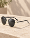 Black and gold round sunglasses with dark lenses resting on a sunlit limestone surface.